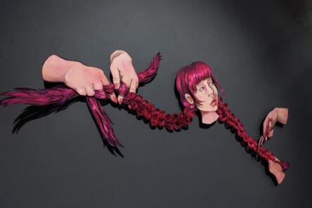 A Defiance in Pink is a mixed media wall-mounted construction of a girl with very long pigtails. The pigtail to the viewer's left is being braided by two hands while the pigtail on the viewer's right is being cut by two hands holding a pair of scissors.
