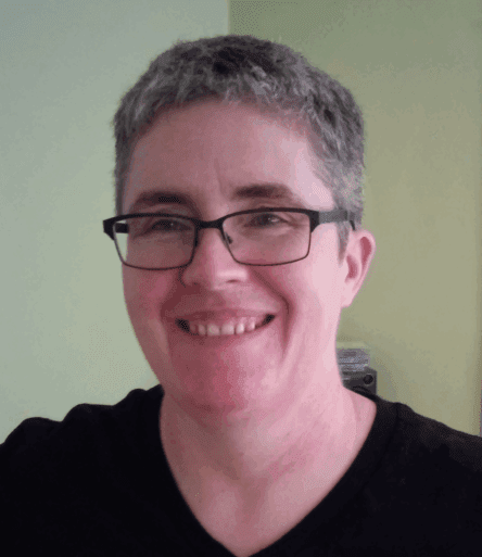 Dr. Sinead shown smiling and wearing a black shirt with black framed glasses