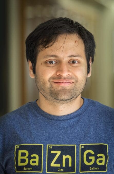 Dr. Ray is pictured with black hair, smiling, in a blue shirt
