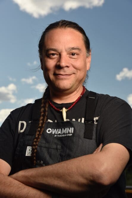 Chef Sean Sherman wearing an apron from his restaurant Owamni

