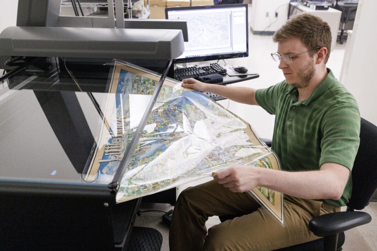A hourly worker places a large map of Little Rock onto a large planetary scanner