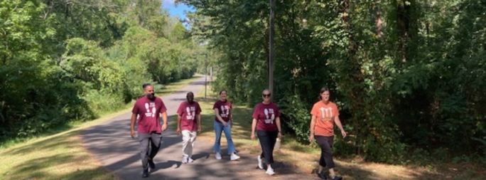 Five people walk along a trail at UA Little Rock. Several are wearing Movement Monday t-shirts.