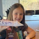 girl scout smiling holding handmade rocket that reads zoom