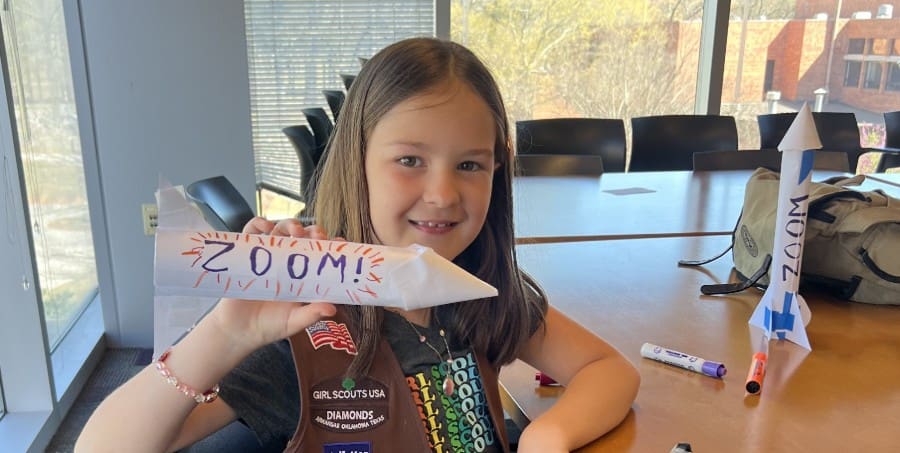 girl scout smiling holding handmade rocket that reads zoom