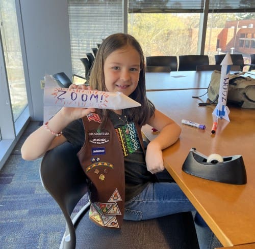 girl scout smiling holding a rocket she made out of paper that says zoom