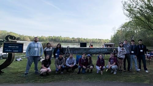 canoe crew posing with their finished concrete canoe with ua little rock painted on the side