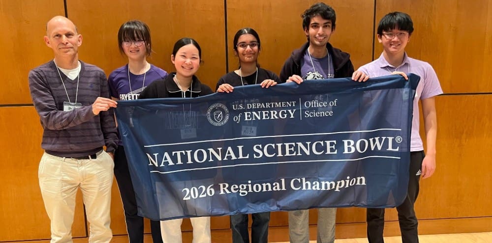 fayetteville high school students smiling and posing with their teach holding the national science bowl banner