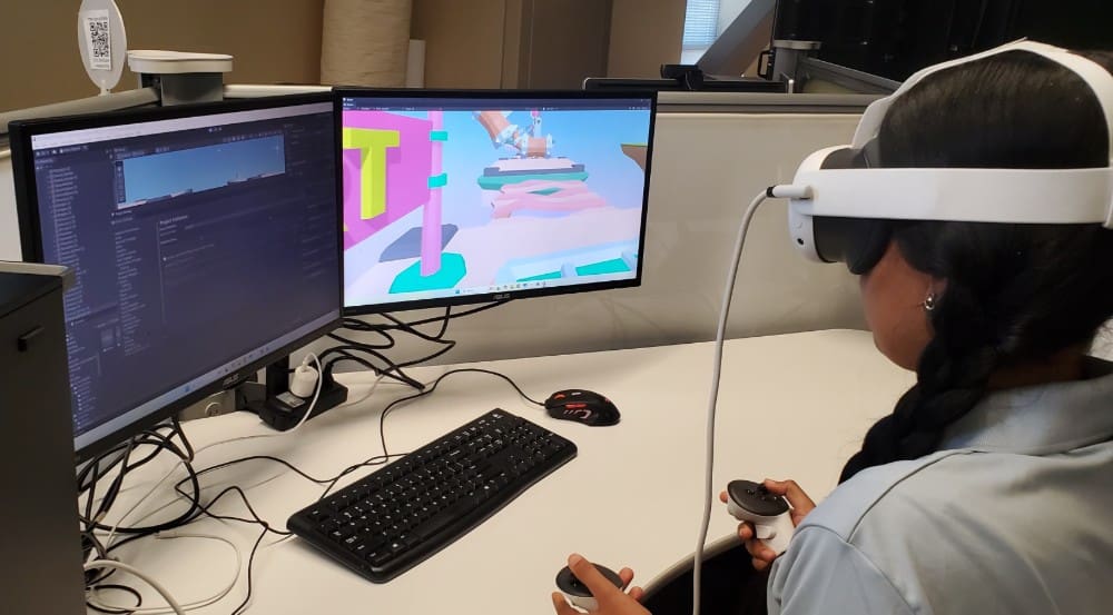 female camper testing her programming code for a virtual reality game using a while VR headset and two hand held controllers