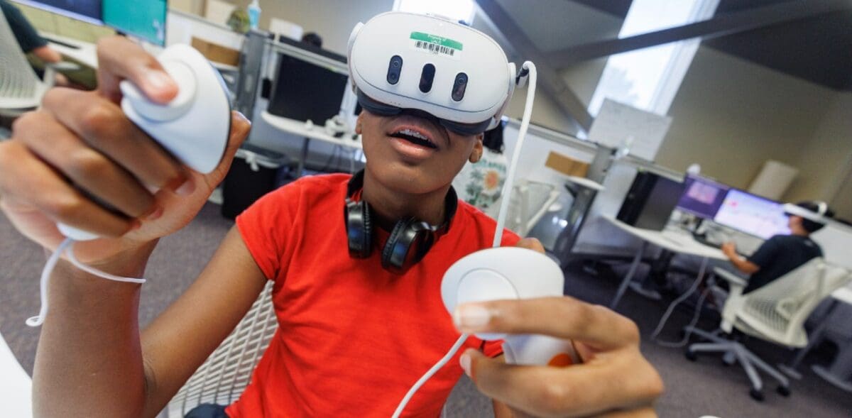 african american male youth interacts with virtual reality device wearing headset and using two hand held controllers