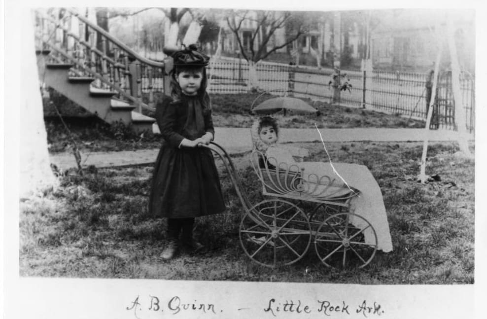 Black and white photo of a young girl pushing a doll in a stroller