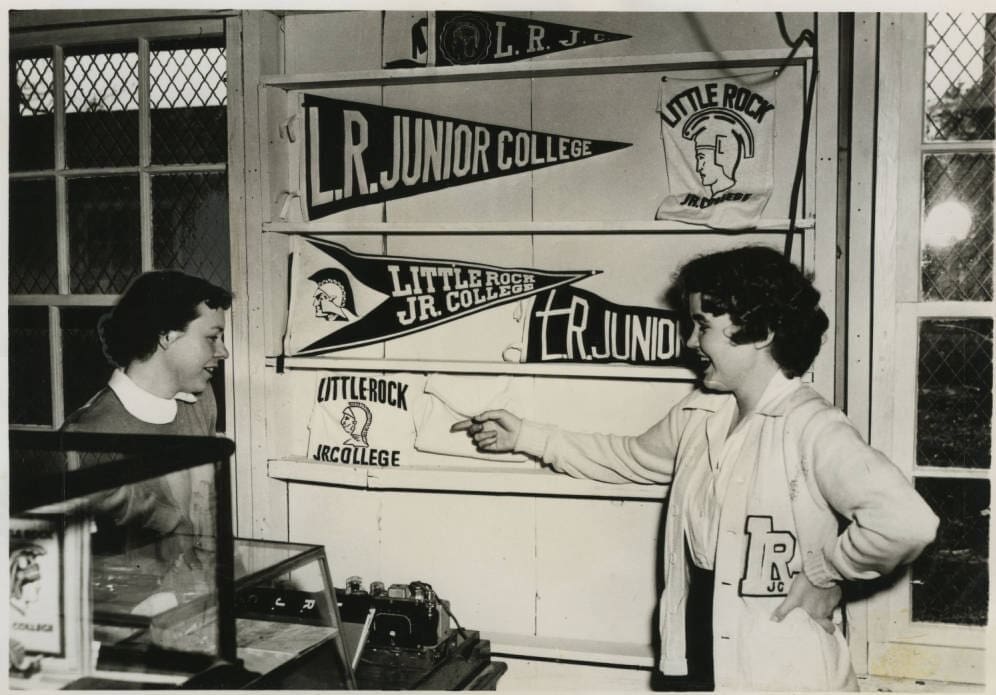 Two girls standing in front of a display case which contains Little Rock Junior College pennants and banners