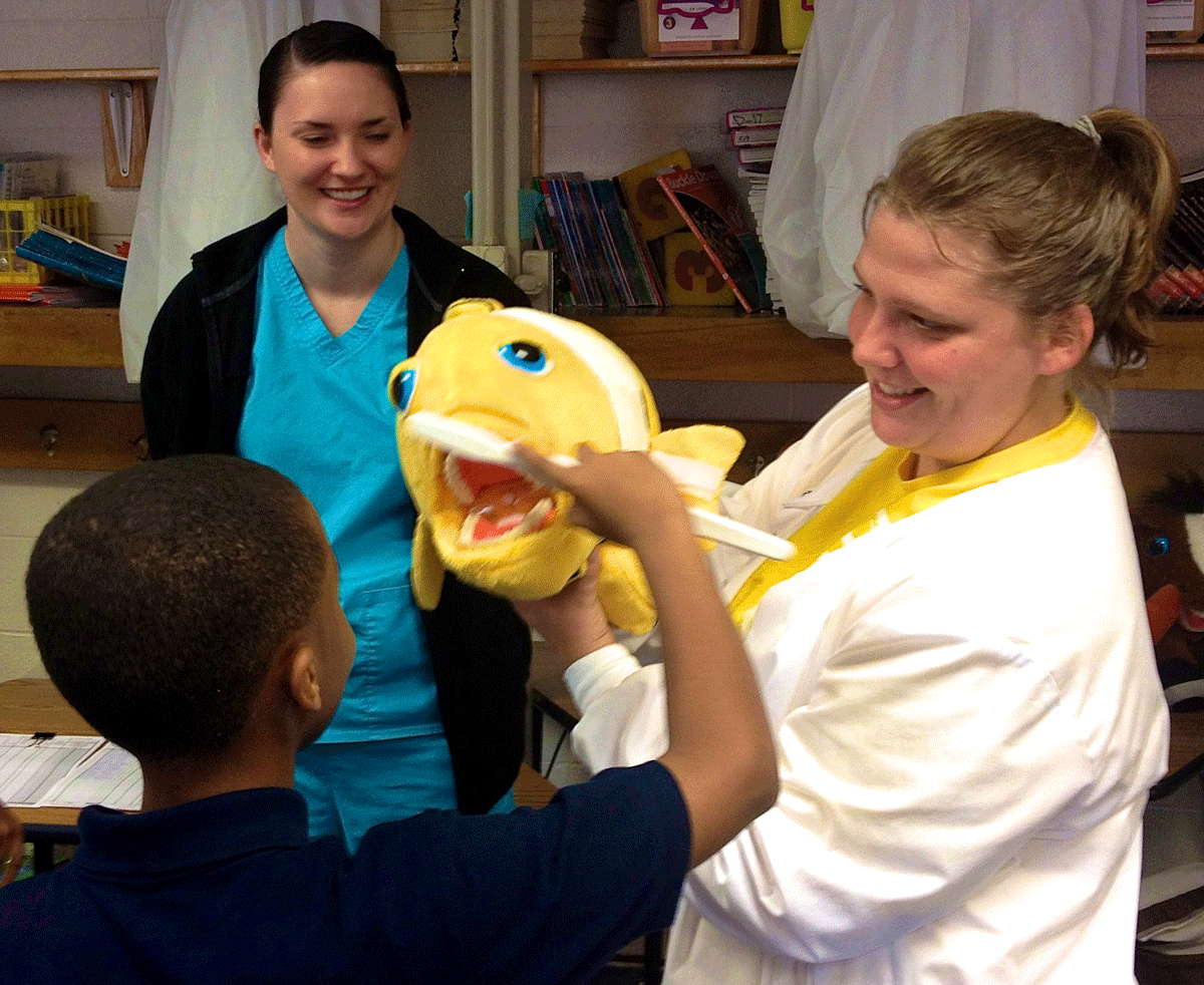 Two dental hygiene students from the University of Arkansas for Medical Sciences show a student how to properly brush his teeth at the Future Smiles Dental Clinic.