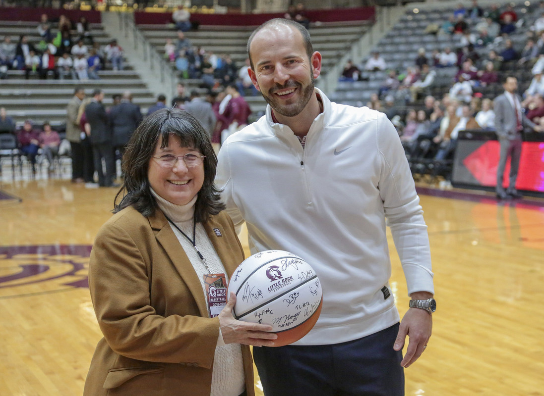 Athletic Director Chasse Conque (right) presents a signed game ball to Interim Executive Vice Chancellor and Provost Christina Drale (left) during a men's basketball game at the Jack Stephens Center. Photo by Benjamin Krain.