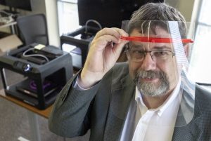 Dr. Larry Whitman, dean of the UA Little Rock College of Engineering and Information Technology, demonstrates the use of a plastic face shield for health professionals working with CODVI-19 patients. The face shields are being made at UA Little Rock by 3D printers. Photo by Ben Krain.