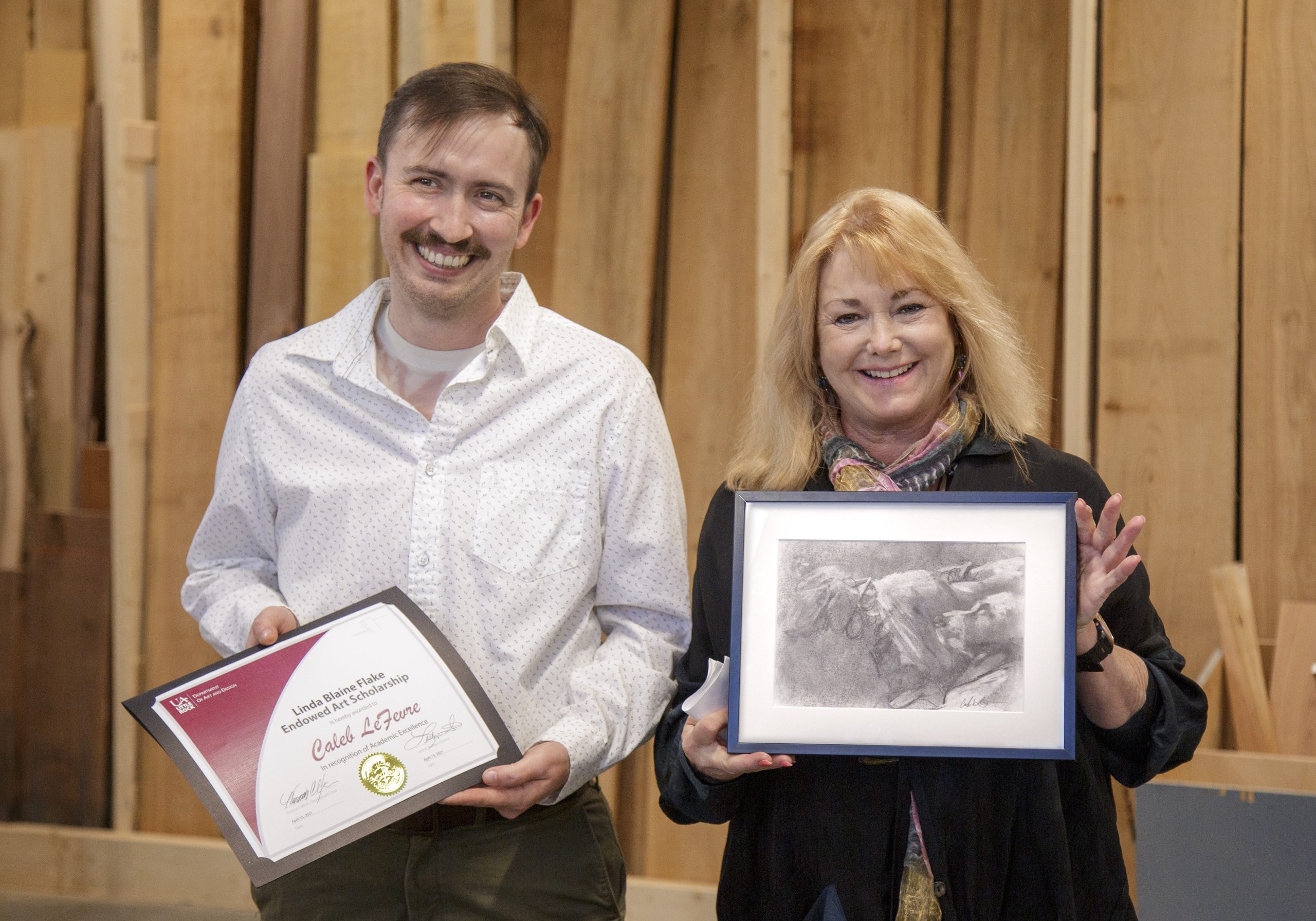 UA Little Rock studio art major Caleb LeFevre, left, was awarded the Linda Blaine Flake Endowed Art Scholarship by philanthropist Lesley Shallom during an event at the Windgate Center for Art + Design in celebration of World Art Day. Shellam is holding one of LeFevre's charcoal art works.