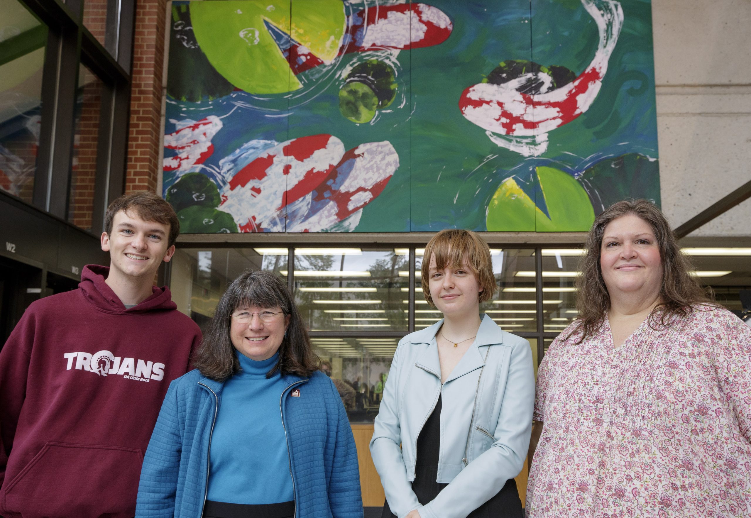 UA Little Rock student artist Emma Chambers, center right, poses in front of her winning mural with Student Government Association president Landon McKay, left, Chancellor Christy Drale center left, and Nancy Hamilton, Faculty Senate Building and Grounds committee member, far right, during a dedication ceremony for the mural at the Ottenheimer Library on campus. Chambers, a junior Bachelor of Fine Arts major with a concentration in painting, won the first student mural competition at the University of Arkansas at Little Rock. The Student Government Association, in conjunction with the Faculty Senate Building and Grounds committee, created the mural contest open to all UA Little Rock students. Chambers received more than 750 votes and $1000 for her design of swimming koi fish.