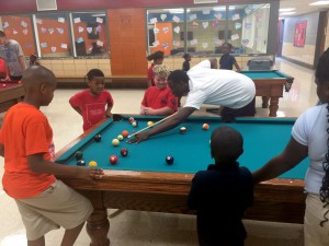 A Trojan athlete shoots pool with youths during a service project