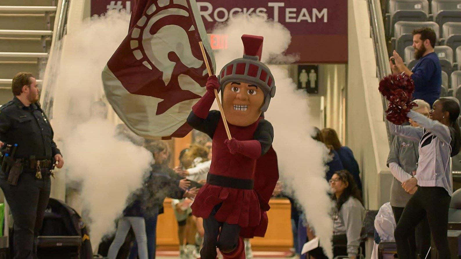 The Trojan mascot waves UA Little Rock's flag at the state of a basketball game.