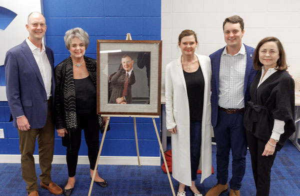 The Clark family standing with the portrait of William "Bill" Clark.