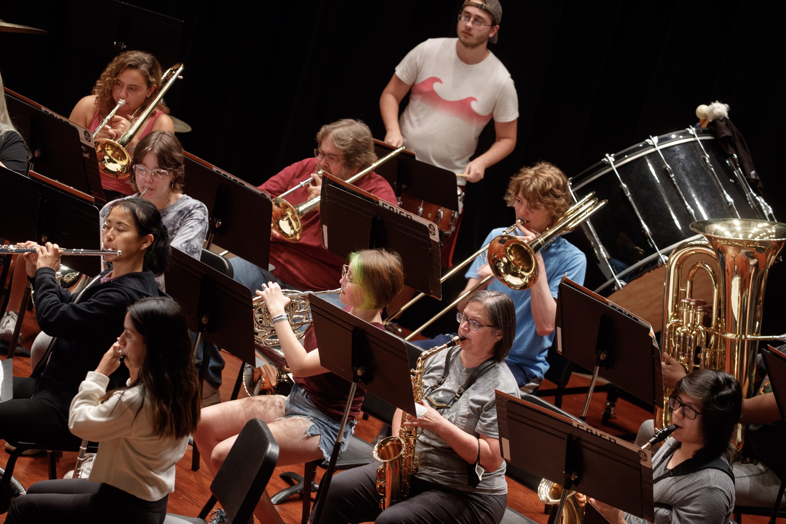 Students play a number of instruments as they look at sheet music on a stage.