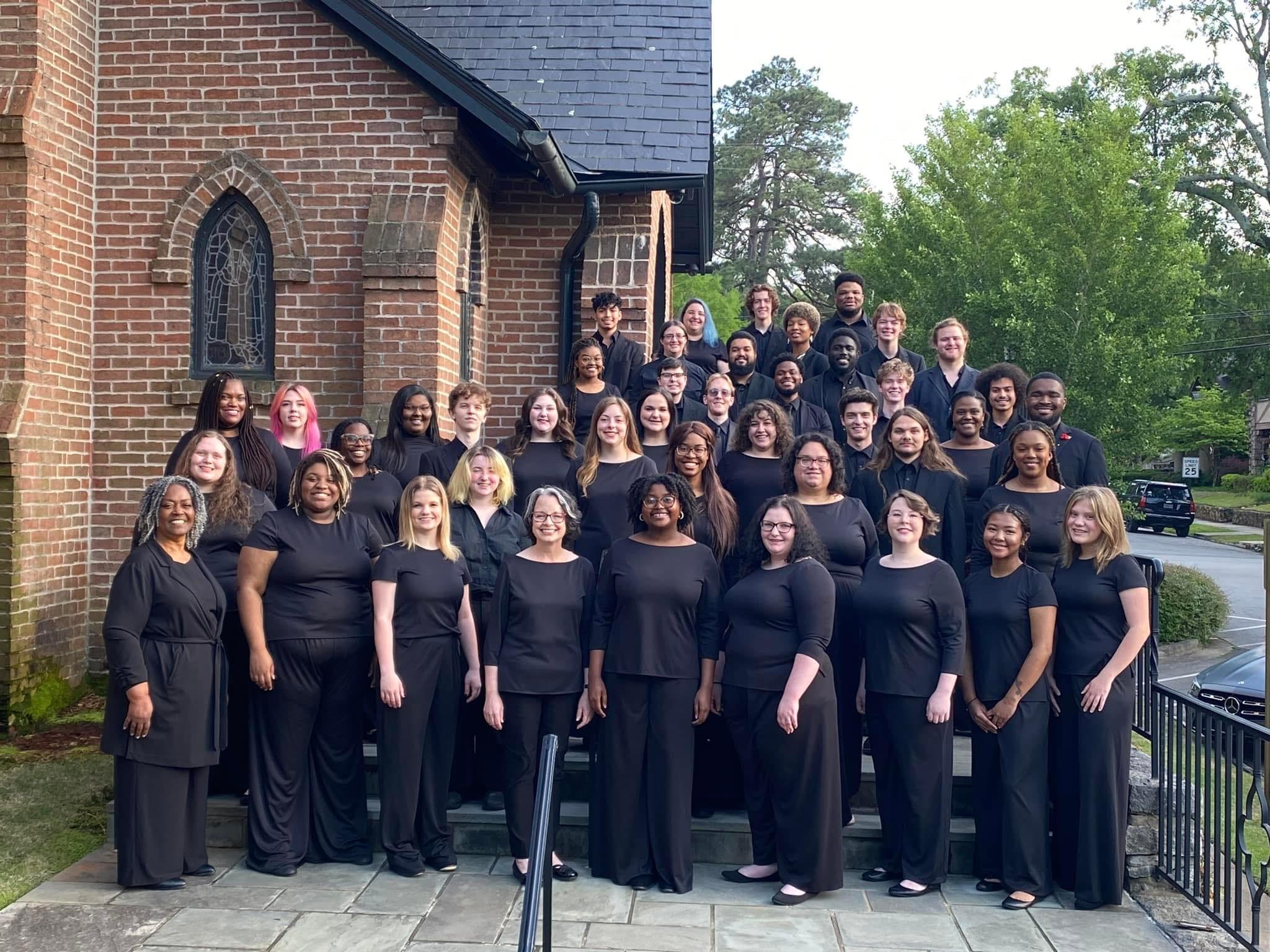 Choir students pose in a line outside of a church for a photo.