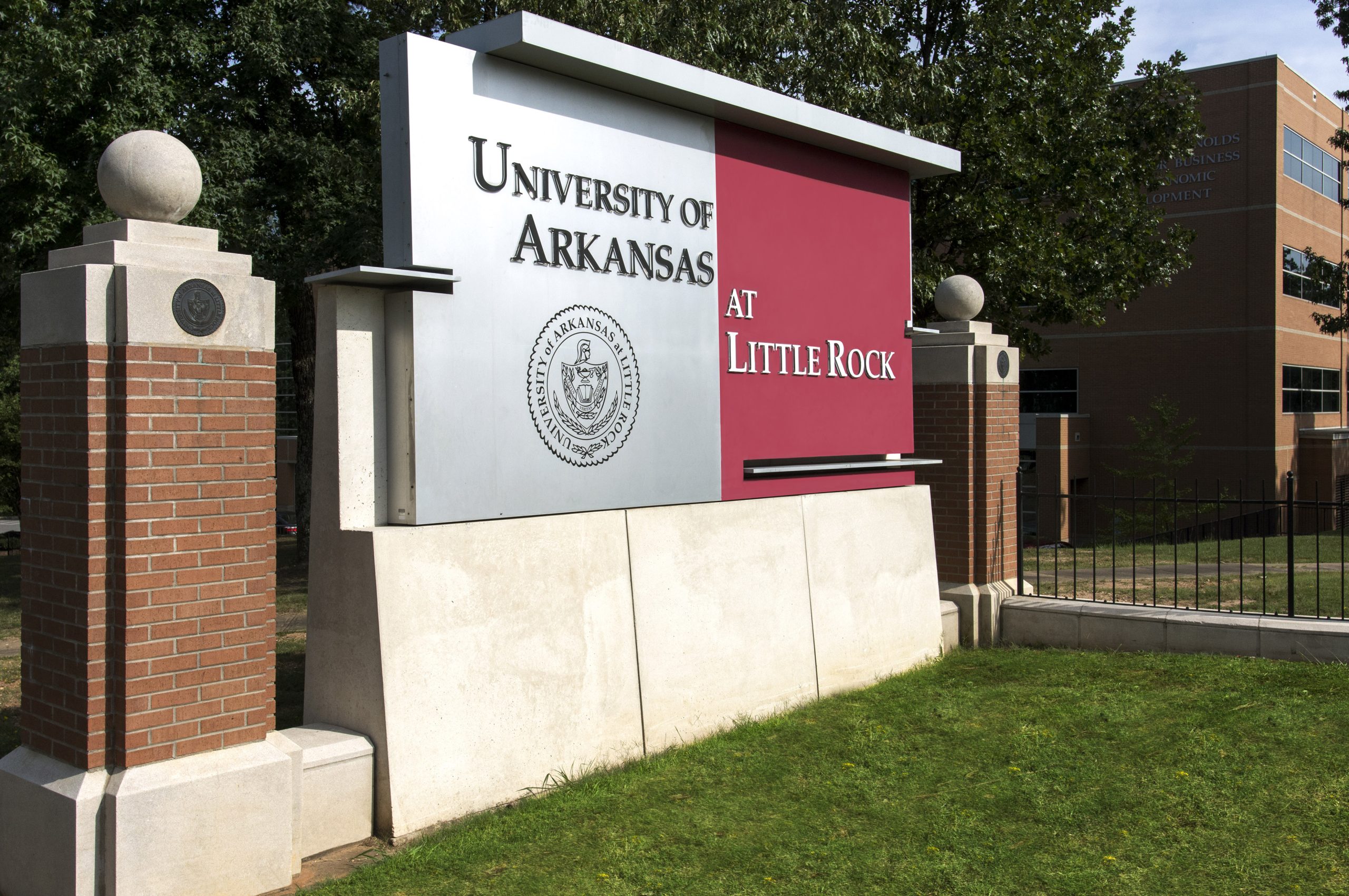 An image of a sign that says University of Arkansas at Little Rock with the university's seal. The left side is grey, and the right side is red with two posts on either side.