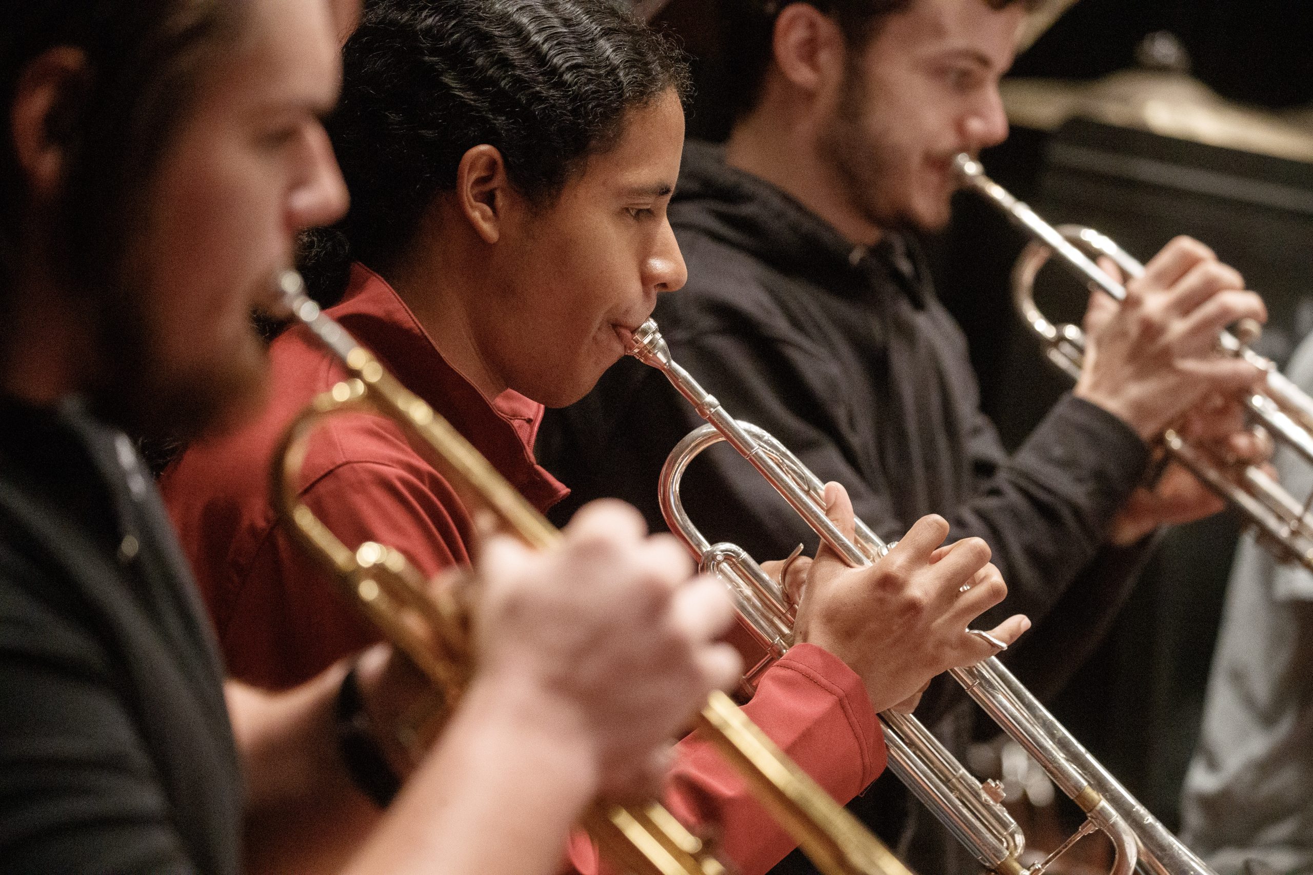 Three students stand next to each other, each playing the trumpet.