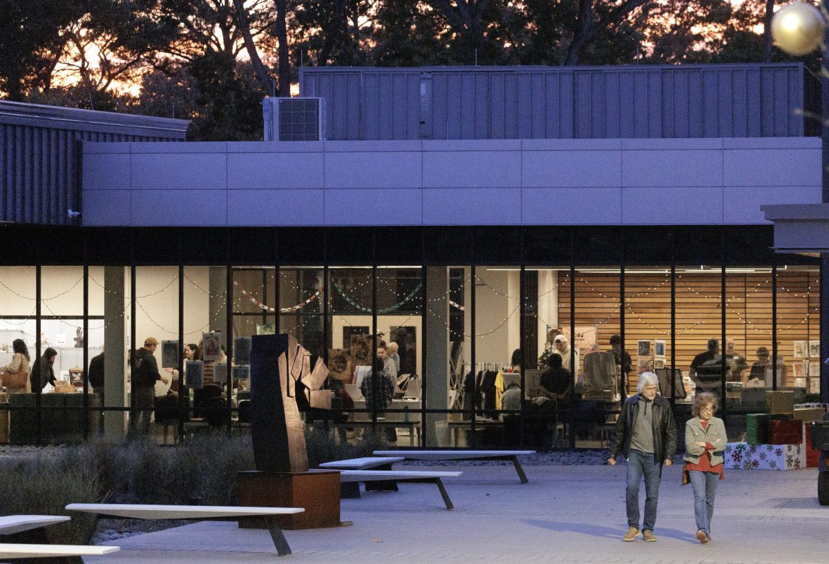 Two people walk outside the Windgate Center of Art + Design. The glass windows show a large crowd gathered in the building.