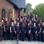 Choir students pose in a line outside of a church for a photo.