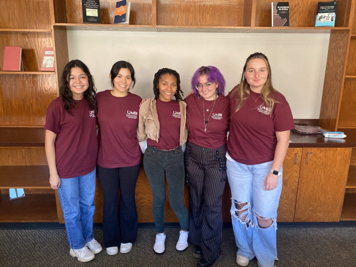 Five students pose and smile for a photo wearing matching t-shirts.