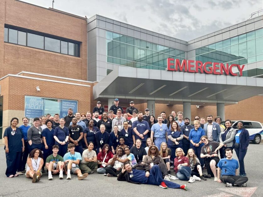Students and healthcare professionals pose for a photograph in front of an emergency department.