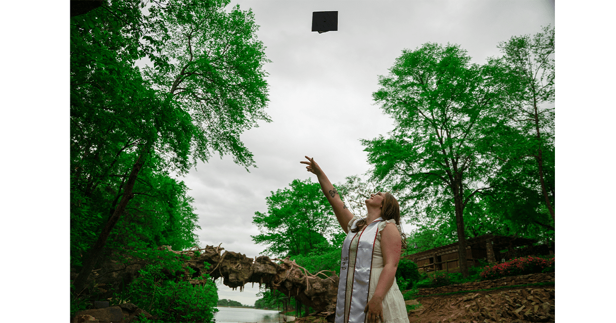 Grace Wilson tosses her graduation cap into the air in a forest.