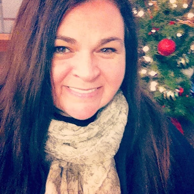 Tracy Crain in front of Christmas tree decorated with lights and ornaments.