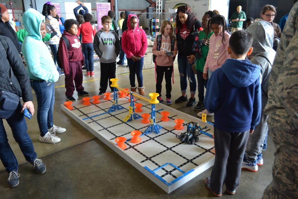 students engaging with science activity - elementary age children standing around a large board that has a constructed element to demonstrate engineering principles