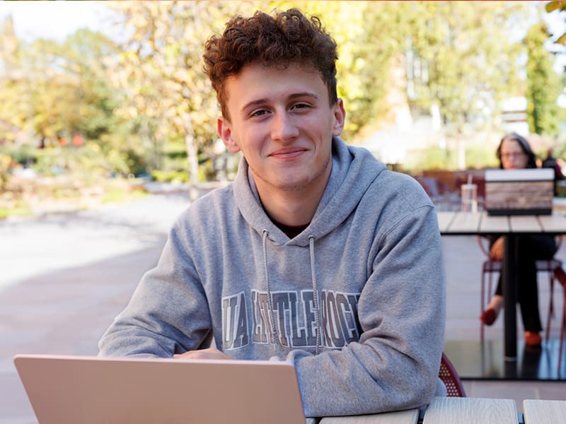 Male student sitting outside working on his laptop.