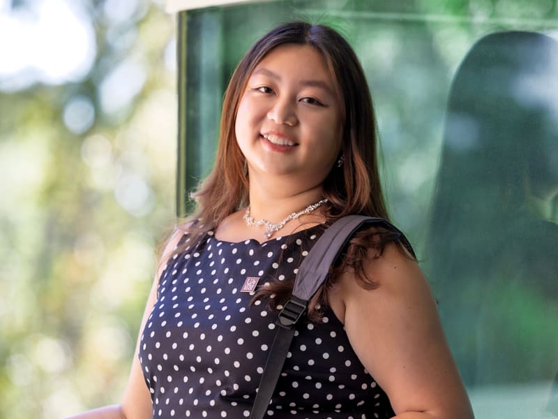 Female student standing next to windows.
